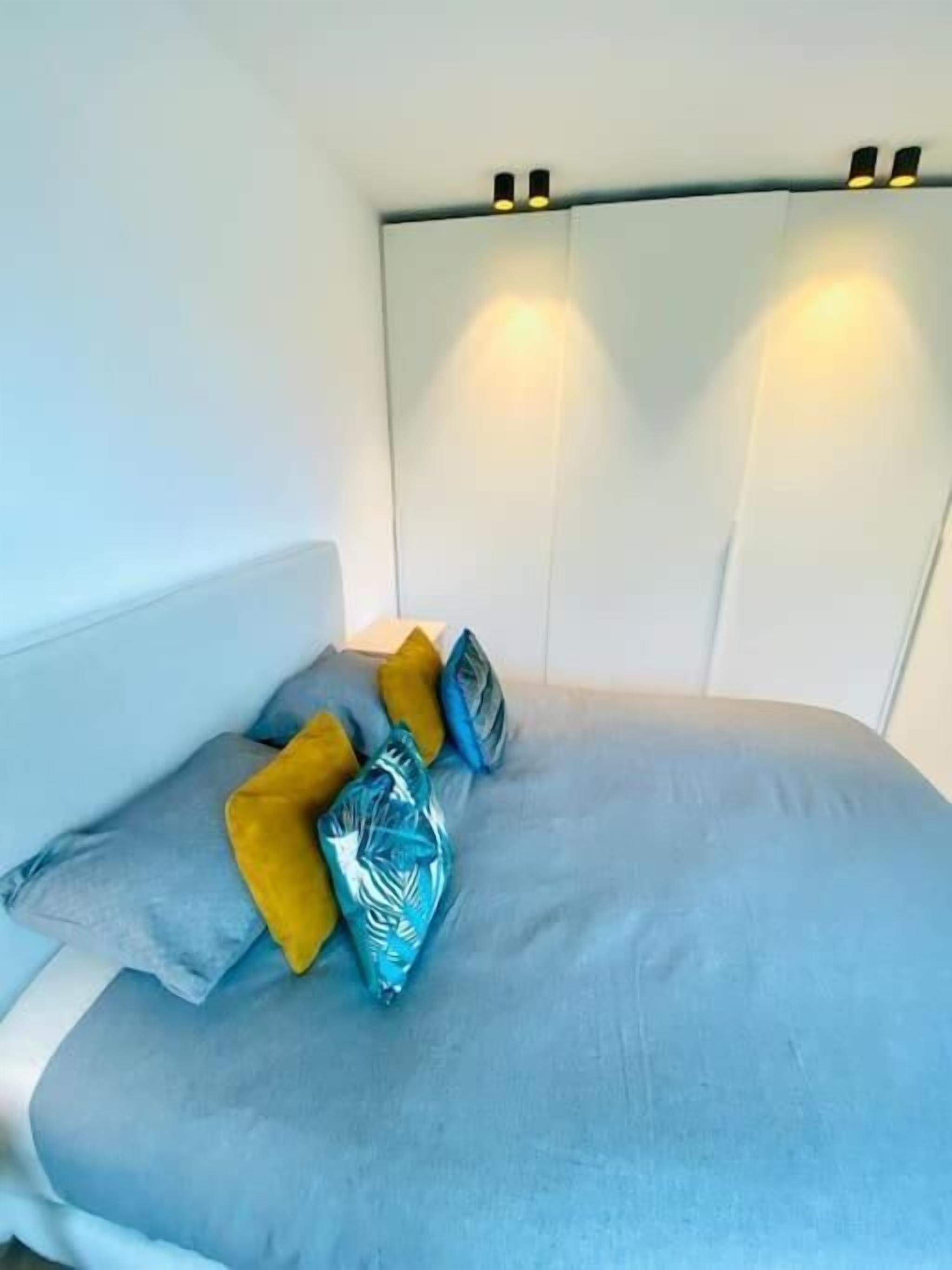 Un lit avec un matelas bleu clair, une tête de lit blanche et trois coussins décoratifs aux couleurs jaune, bleu et blanc.
