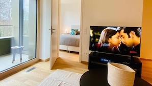 Moderni olohuone, jossa on suuri televisio jalustalla, sohva ja lasiovi, joka johtaa parvekkeelle.