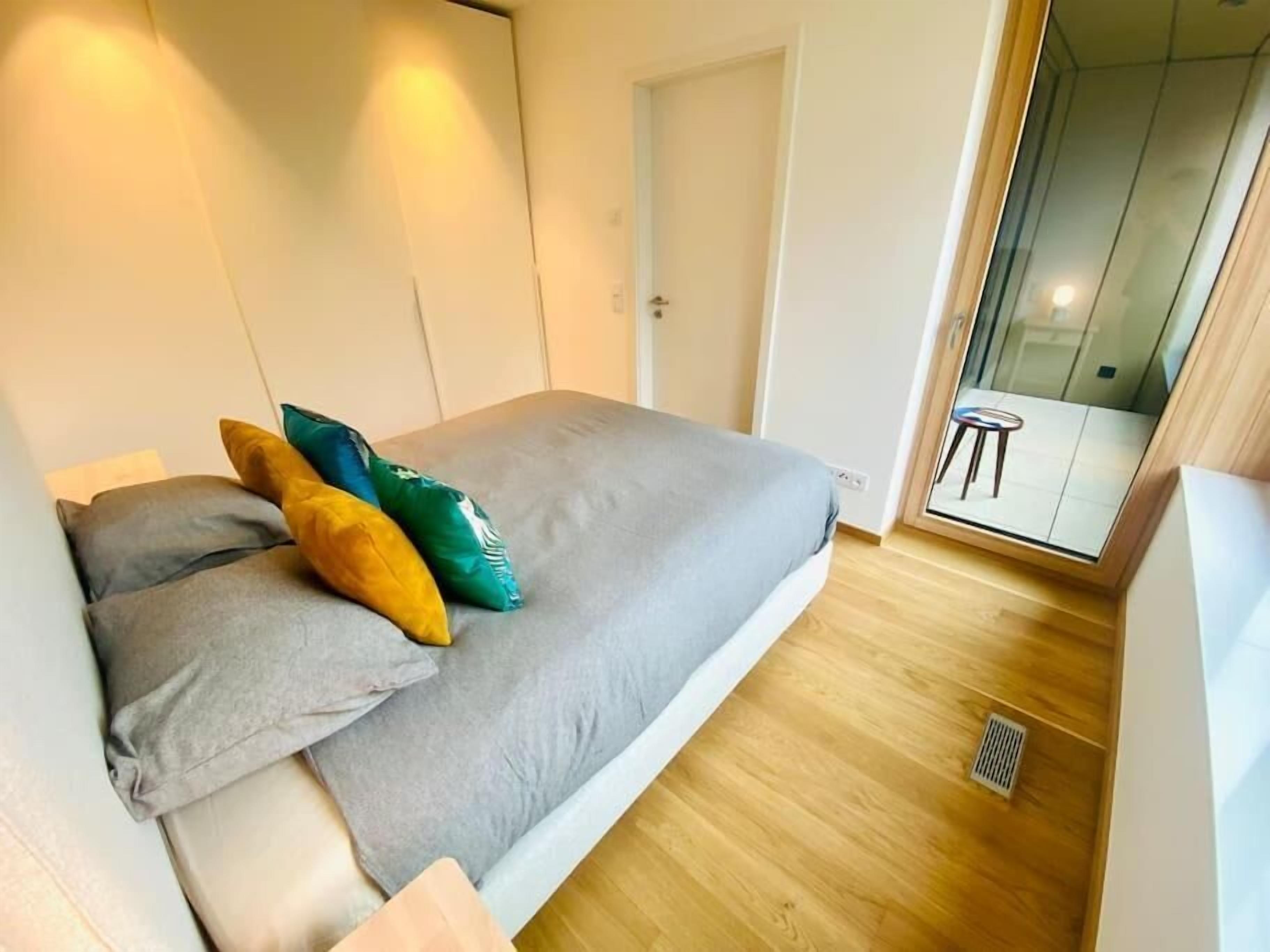 Un dormitorio moderno con cama, almohadas y un ventanal corredero que da a un balcón.