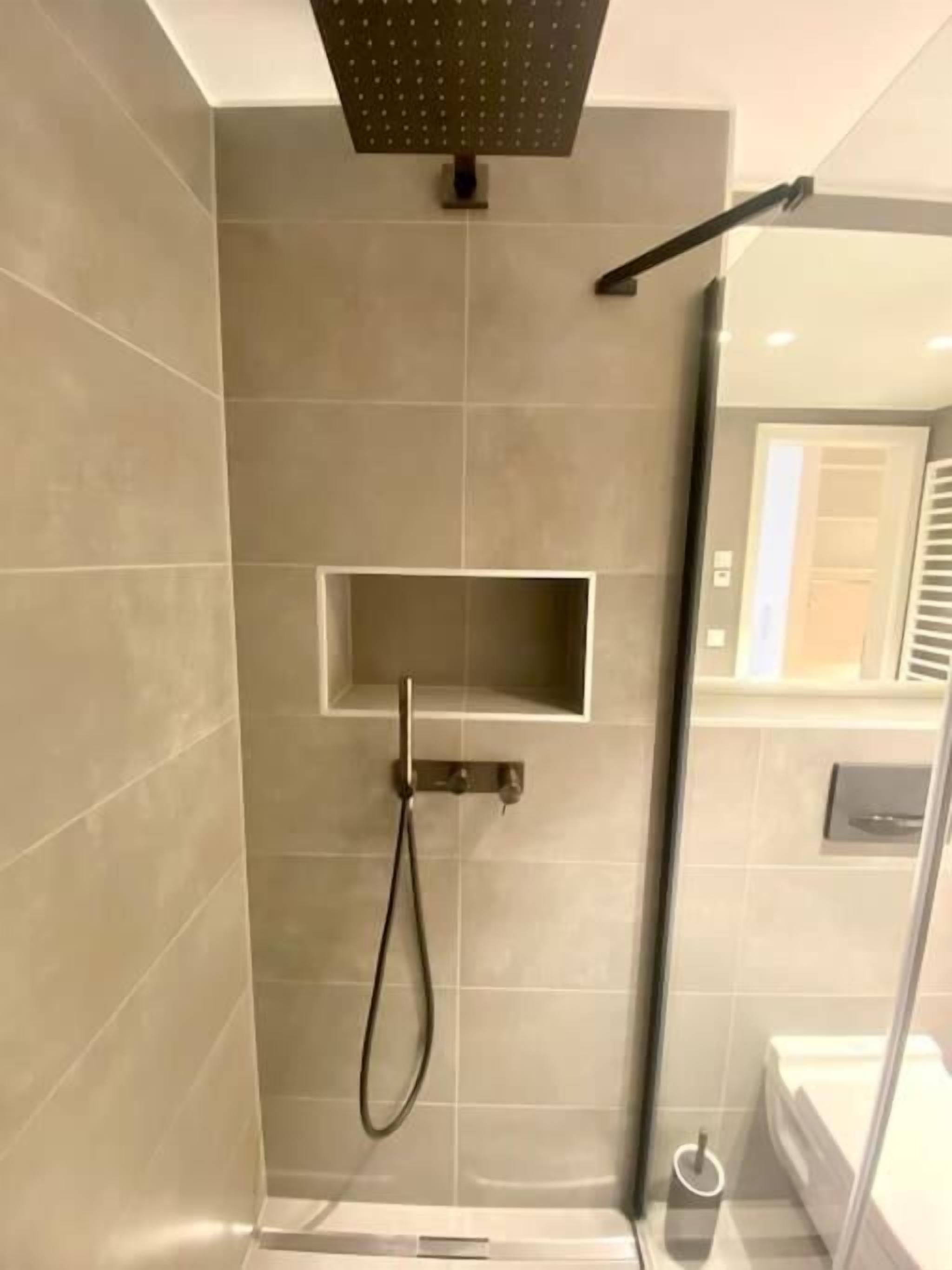 A modern bathroom with a shower, a small shelf, and a toilet.