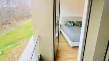 A modern bedroom with a large window, a bed, and a view of a green landscape.