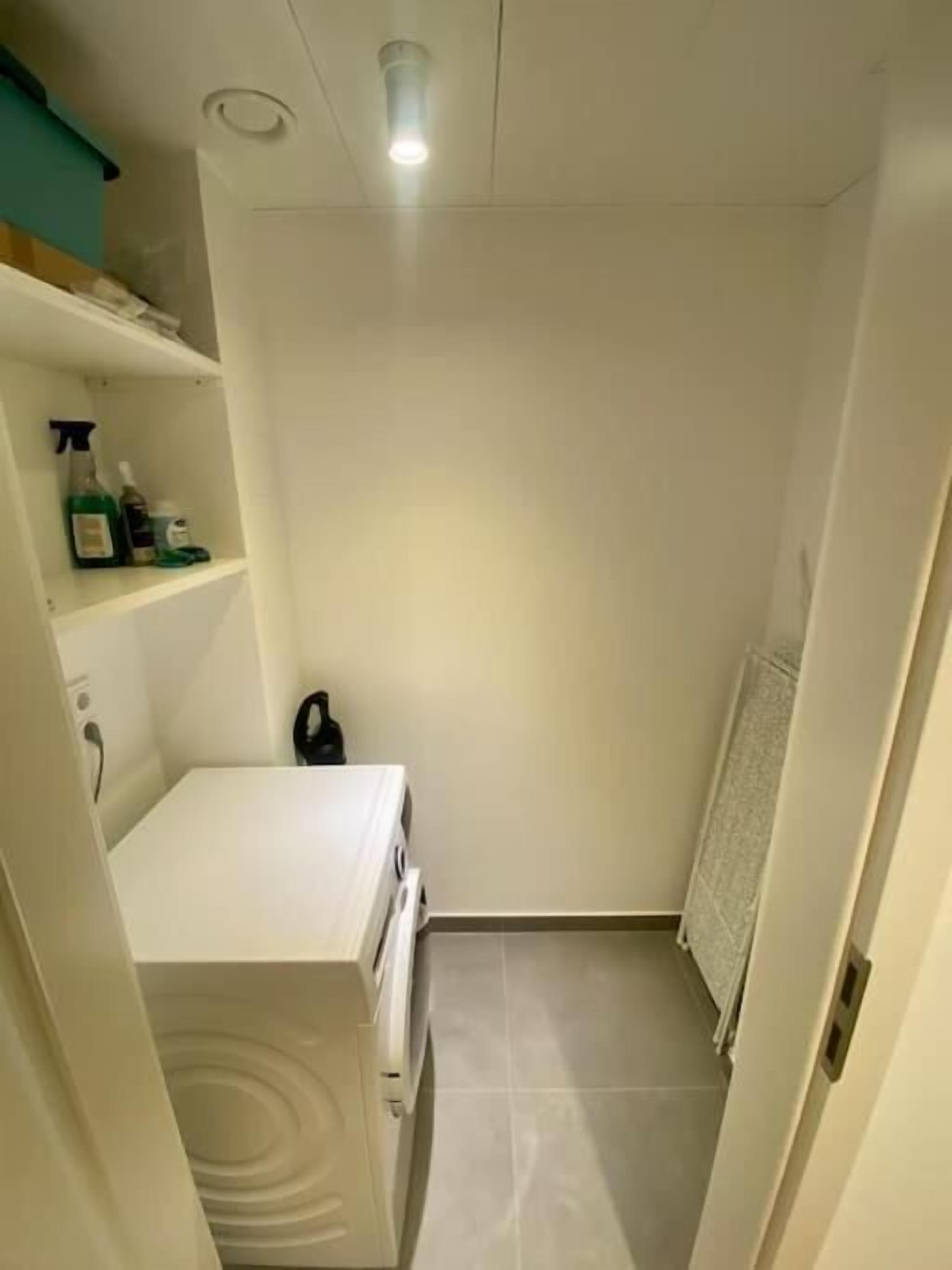 A small, narrow bathroom with a white sink, a mirror, and a shelf with toiletries.
