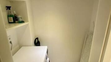 A small, narrow bathroom with a white sink, a mirror, and a shelf with toiletries.
