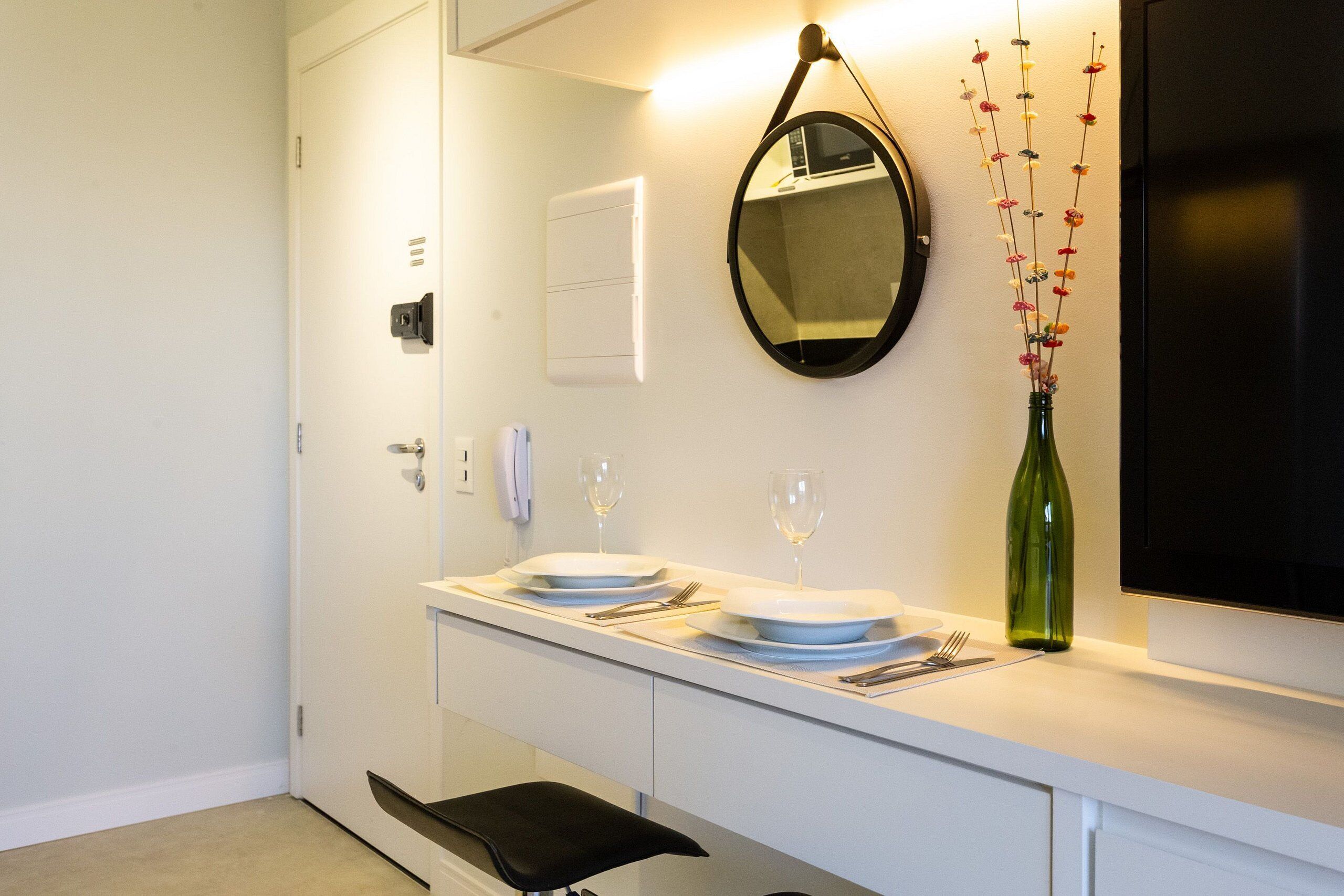 A modern bathroom with a white vanity, a black sink, a mirror, and a green vase with flowers.