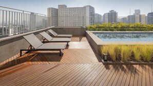Eine Dachterrasse mit Holzboden, Liegestühlen, einem Swimmingpool und Blick auf die Stadt.