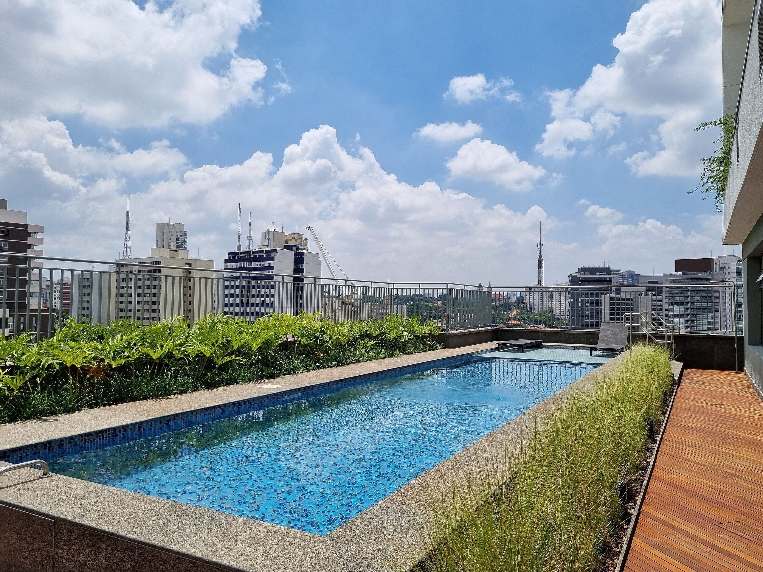Piscina en la azotea con vistas a la ciudad, rodeada de vegetación y una terraza de madera.