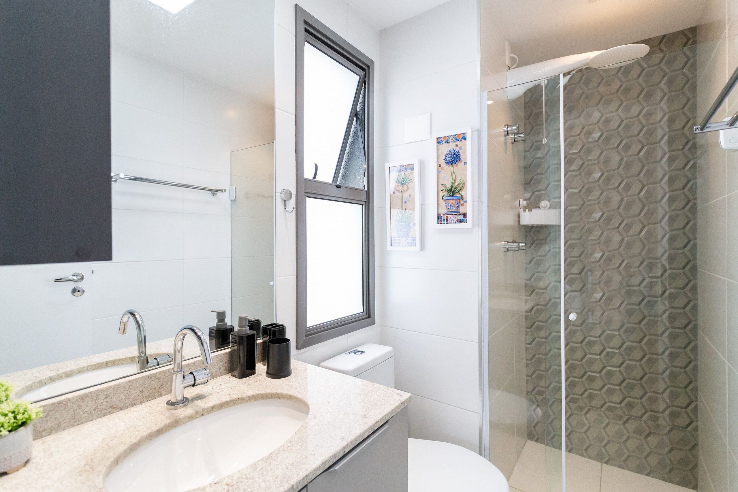 A modern bathroom with a large window, a shower with a hexagonal tile pattern, and a sink with a countertop.