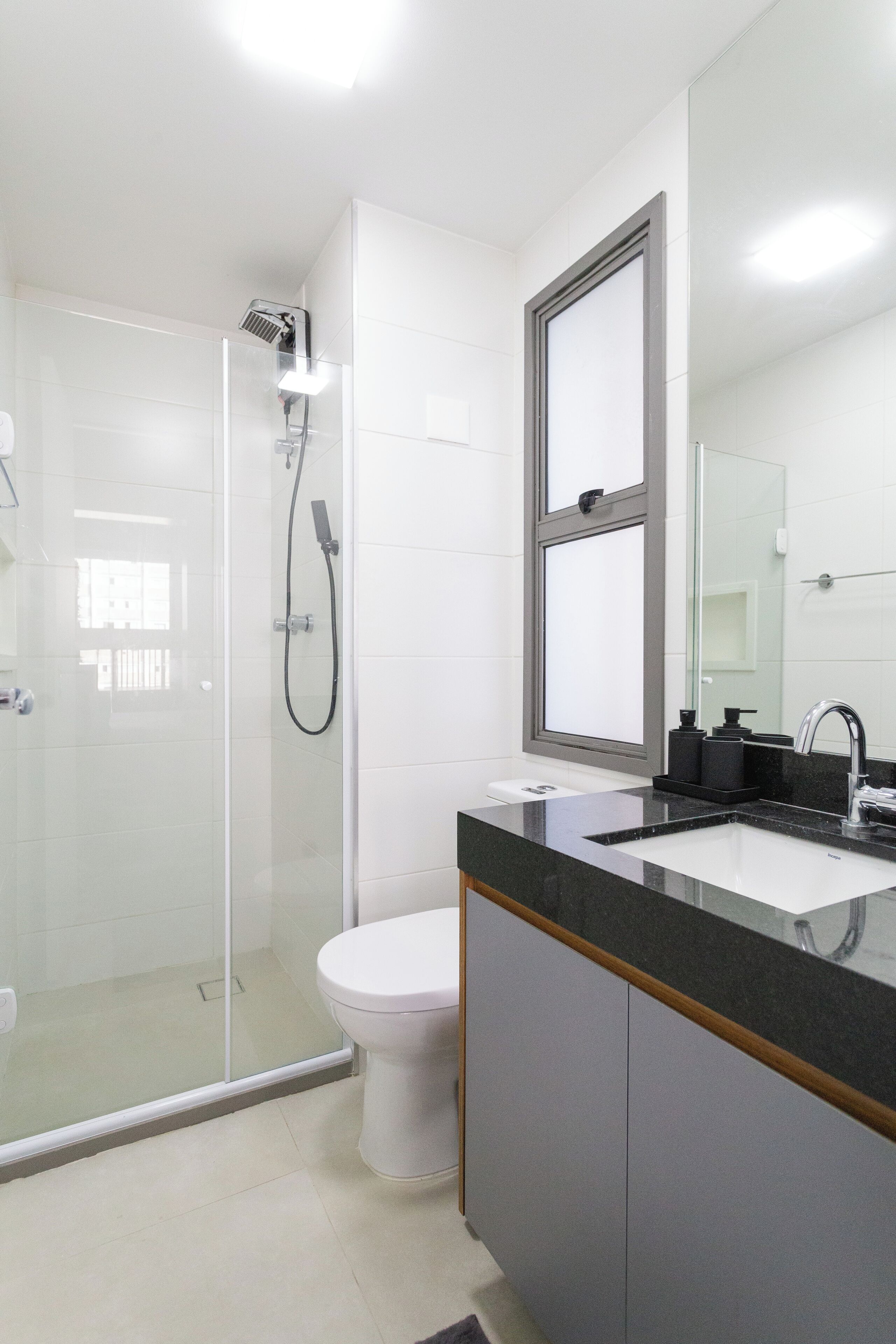Une salle de bain moderne avec une douche à parois de verre, des toilettes blanches et un plan de toilette noir avec un lavabo.
