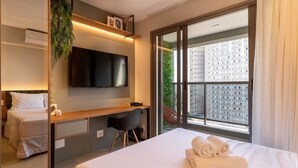 Ein Hotelzimmer mit Bett, Schreibtisch, Stuhl, Fernseher und einem großen Fenster mit Blick auf Gebäude.