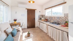 Una cocina moderna con puerta de madera, comedor con mesa y sillas, y sala de estar con sofá y cojines.