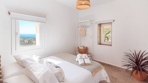 Un dormitorio con una cama, una ventana con vistas, una mesita de noche, una lámpara colgante y una planta en maceta.