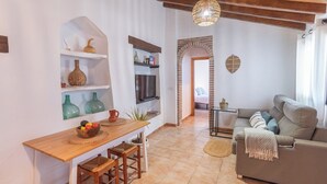 Una sala moderna con un sofá, una mesa de comedor con sillas, una zona de cocina con televisor y un arco de ladrillo que conduce a otra habitación.