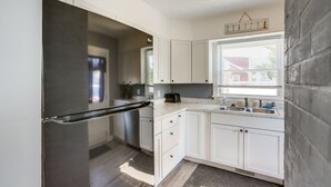 A modern kitchen with white cabinets, a stainless steel refrigerator, and a window with blinds. - Dog-Friendly Port Clinton Home: Walk to Lake Erie! (Port Clinton)