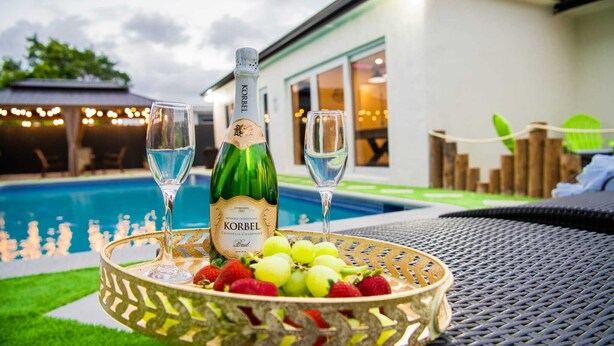 A bottle of Korbel champagne, two glasses, and a fruit basket on a table by a pool. - Luxury Miami Villa/Nr Beach/Heated POOL/BBQ/Firepit/Games/Minigolf/Basketball (Miami)