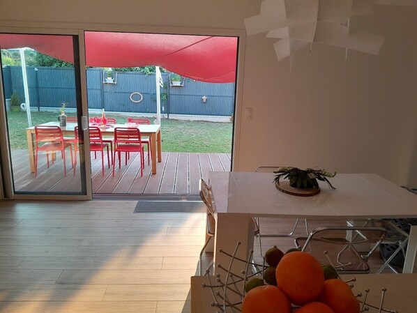 Une pièce dotée d’une porte-fenêtre coulissante donnant sur un patio extérieur agrémenté d’un parasol rouge, d’une terrasse en bois et d’une clôture bleue.
