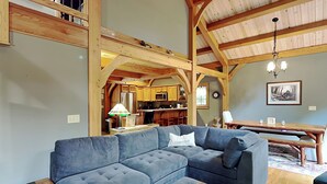 Un amplio salón con un sofá seccional grande, piso de madera y vigas de madera a la vista.