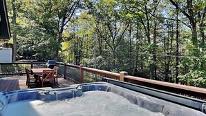Tinaco de hidromasaje en una terraza de madera con vista a un bosque.