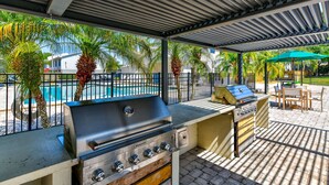 An outdoor patio with a grill station, a pool, and a covered seating area. - Cozy Townhome| Moffitt| Pool| Gym| Fast WiFi| 2B2B (Tampa)