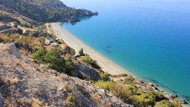 A coastal landscape with a beach, rocky terrain, and sparse vegetation.