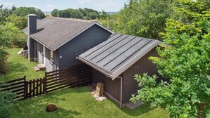 Een rustieke chalet met een schuin dak, schoorsteen en een klein terras met buitenmeubels.