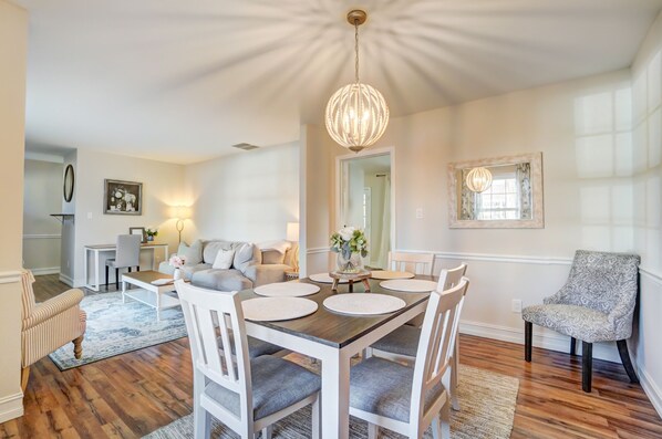 Un coin repas avec une table en bois, des chaises blanches et un lustre.