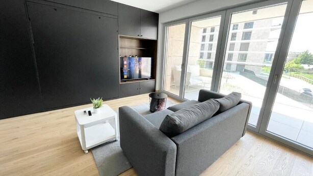 A modern living room with a grey sofa, a small white side table, and a black cabinet. - Luxury 2023 Flat -Center Terrace Parking (Luxembourg City)