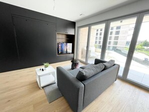 A modern living room with a grey sofa, a small white side table, and a black cabinet. - Luxury 2023 Flat -Center Terrace Parking (Luxembourg City)