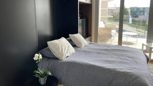 A modern bedroom with a large bed, a TV, and a balcony with a view of buildings. - Luxury 2023 Flat -Center Terrace Parking (Luxembourg City)