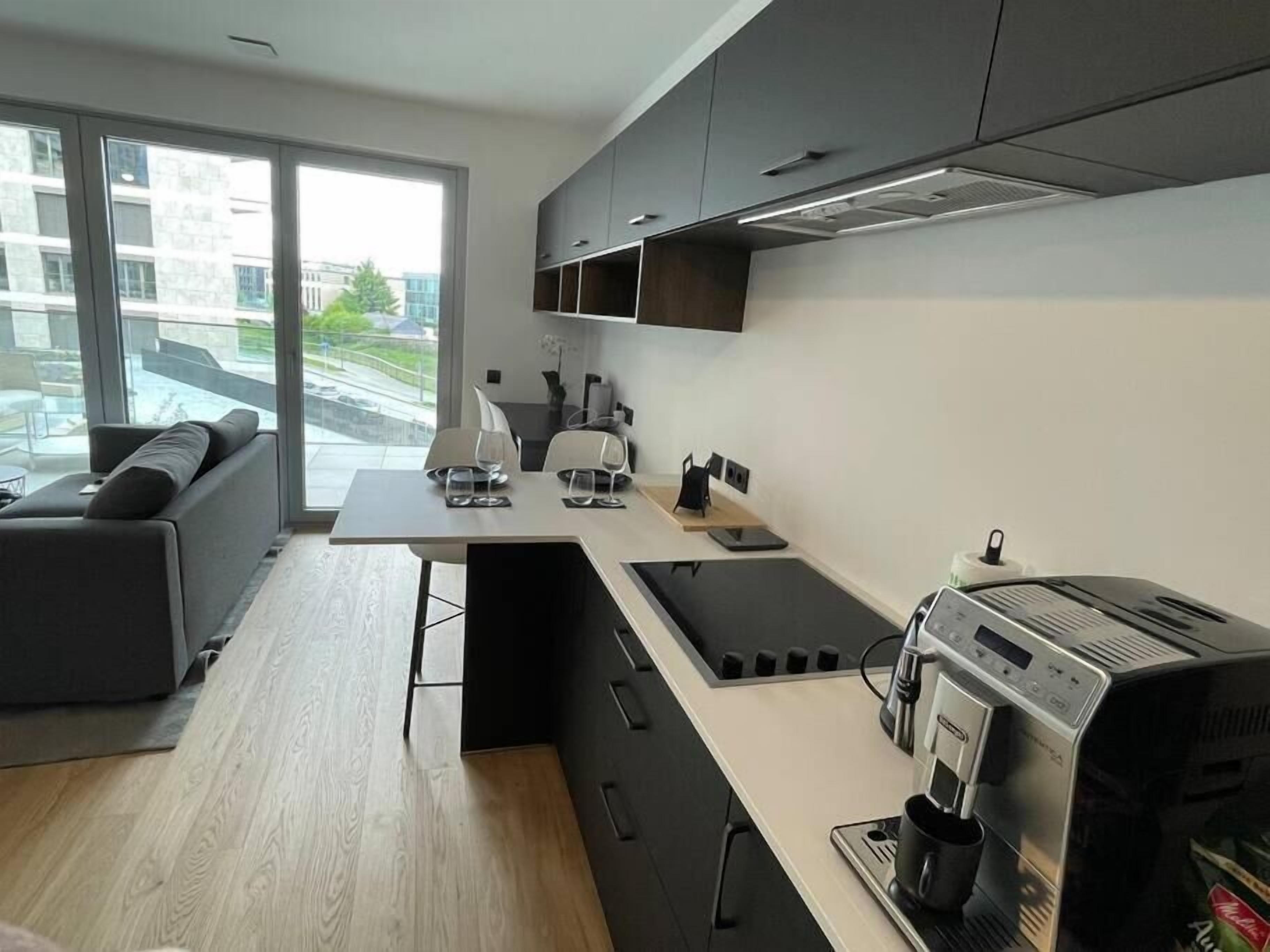 Una cocina moderna con cafetera espresso integrada, un comedor con sofá y ventanas amplias con vistas a la ciudad.