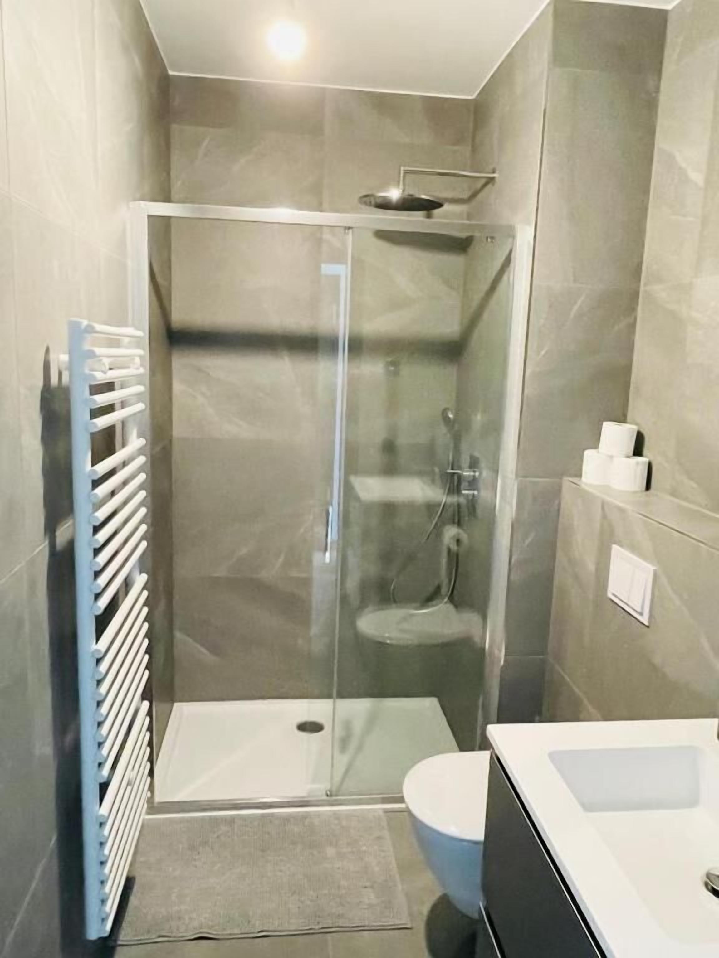 A modern bathroom with a glass-enclosed shower, a white sink, and a toilet.