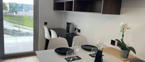 A modern dining area with a table set for two, a potted orchid, and a view of the outside.