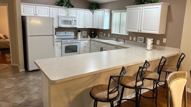 A kitchen with white cabinets, a central island with bar stools, and a refrigerator. - 3 bedroom / 2 bath Courtyard Villa w/ cart! (The Villages)