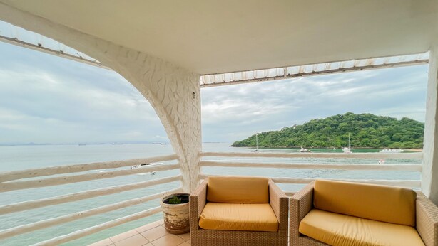 A balcony with wicker furniture and a view of the sea and a green island. - Live an Adventure in Taboga 1 (Provincia de Panamá)