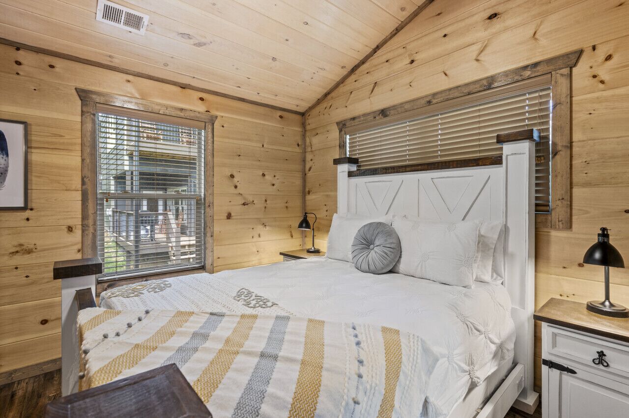 A wooden cabin bedroom with a bed, nightstands, and a window with blinds.