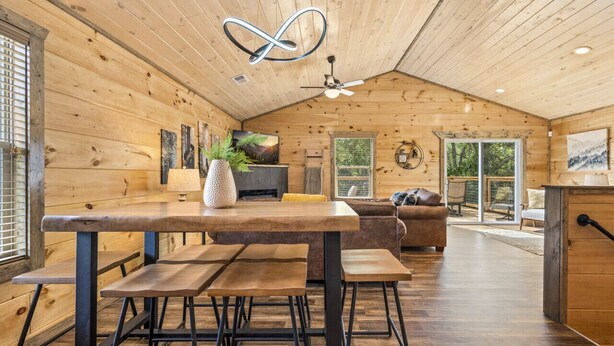 Ein Holzblockhaus-Interieur mit Esstisch, Bänken, einer Couch und einem Deckenventilator.