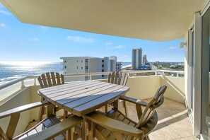 A balcony with a wooden table and chairs, overlooking a beach and buildings.