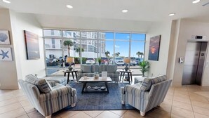 A modern lobby with a large window, two sofas, a coffee table, and a small table with a lamp. - Coastal Elegance Beachfront View (Pensacola)