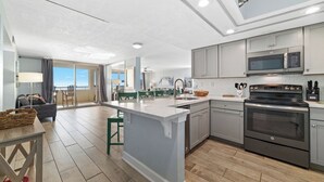 A modern kitchen with grey cabinets, a central island, stainless steel appliances, and a view to the outside. - Coastal Elegance Beachfront View (Pensacola)