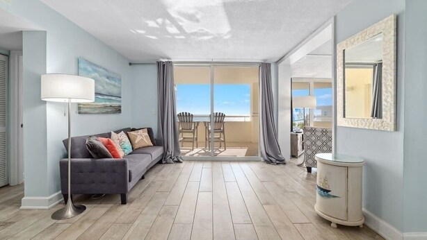 A spacious living room with a grey sofa, a floor lamp, and a view through a glass door to an outdoor patio. - Coastal Elegance Beachfront View (Pensacola)