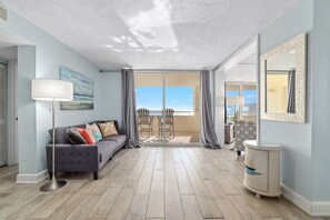 A spacious living room with a grey sofa, a floor lamp, and a view through a glass door to an outdoor patio. - Coastal Elegance Beachfront View (Pensacola)