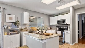 A modern kitchen with white cabinetry, a central island, and a large window providing natural light. - Lg 3 bedroom home with game rm (San Antonio)