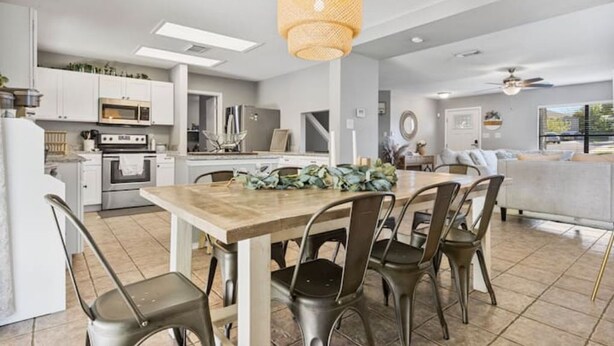 A modern kitchen with white cabinetry, a wooden dining table, and a hanging light fixture. - Lg 3 bedroom home with game rm (San Antonio)