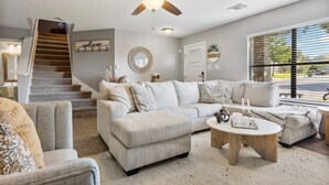 A living room with a sofa, armchairs, a coffee table, a ceiling fan, a staircase, and a large window with blinds. - Lg 3 bedroom home with game rm (San Antonio)
