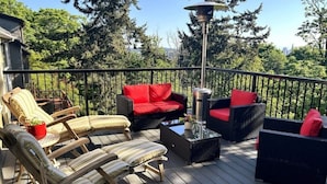 A deck with wicker furniture, red cushions, and a table lamp.