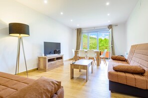 Uma sala de estar moderna com televisão de tela plana, sofá, mesa de centro e um espaço de jantar com cadeiras.