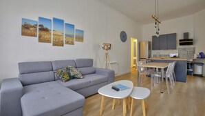 A modern living room with a grey sofa, a coffee table, and a dining area with chairs and a table. There is a kitchen in the background with cabinets and a microwave. - Boulevard de la Plage flat-Arcachon (Arcachon)