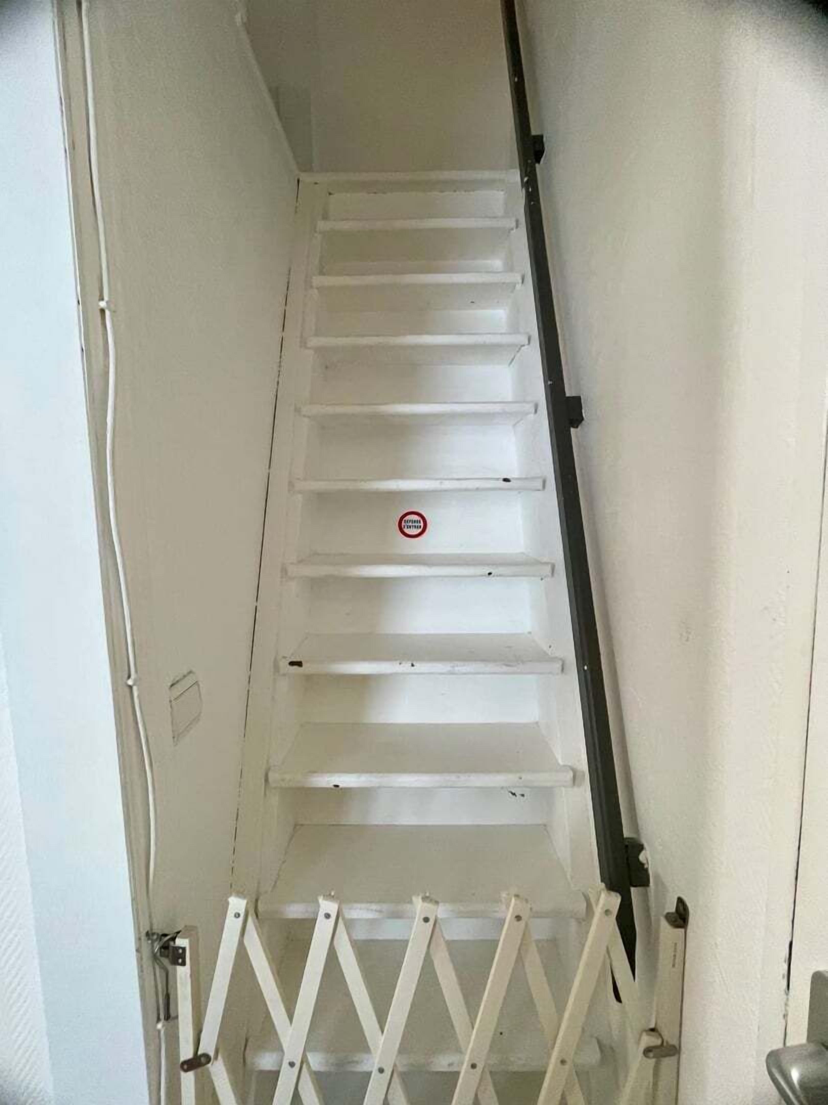 A narrow, enclosed stairwell with a metal banister and a white door at the bottom.