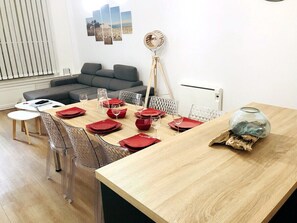Un coin repas avec une table en bois dressée pour quatre personnes, des chaises transparentes et un canapé gris en arrière-plan.