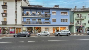 A street view with multi-story buildings, storefronts, and parked cars. - GuestHost - Penthouse Central Apartment (Tarvisio)