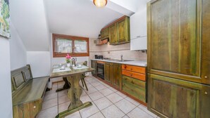 A compact kitchen with wooden cabinets, a dining table, and a bench. - GuestHost - Penthouse Central Apartment (Tarvisio)